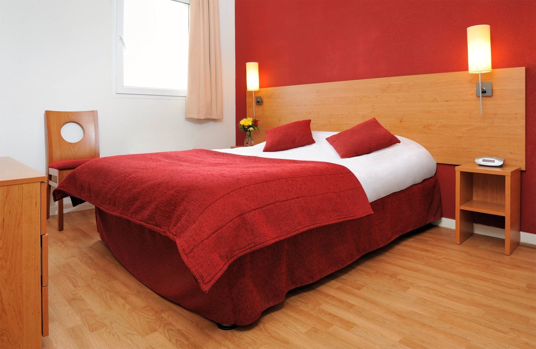Een hotelkamer met een groot bed, een houten hoofdeinde, twee nachtkastjes, een stoel en een raam met gordijnen.
