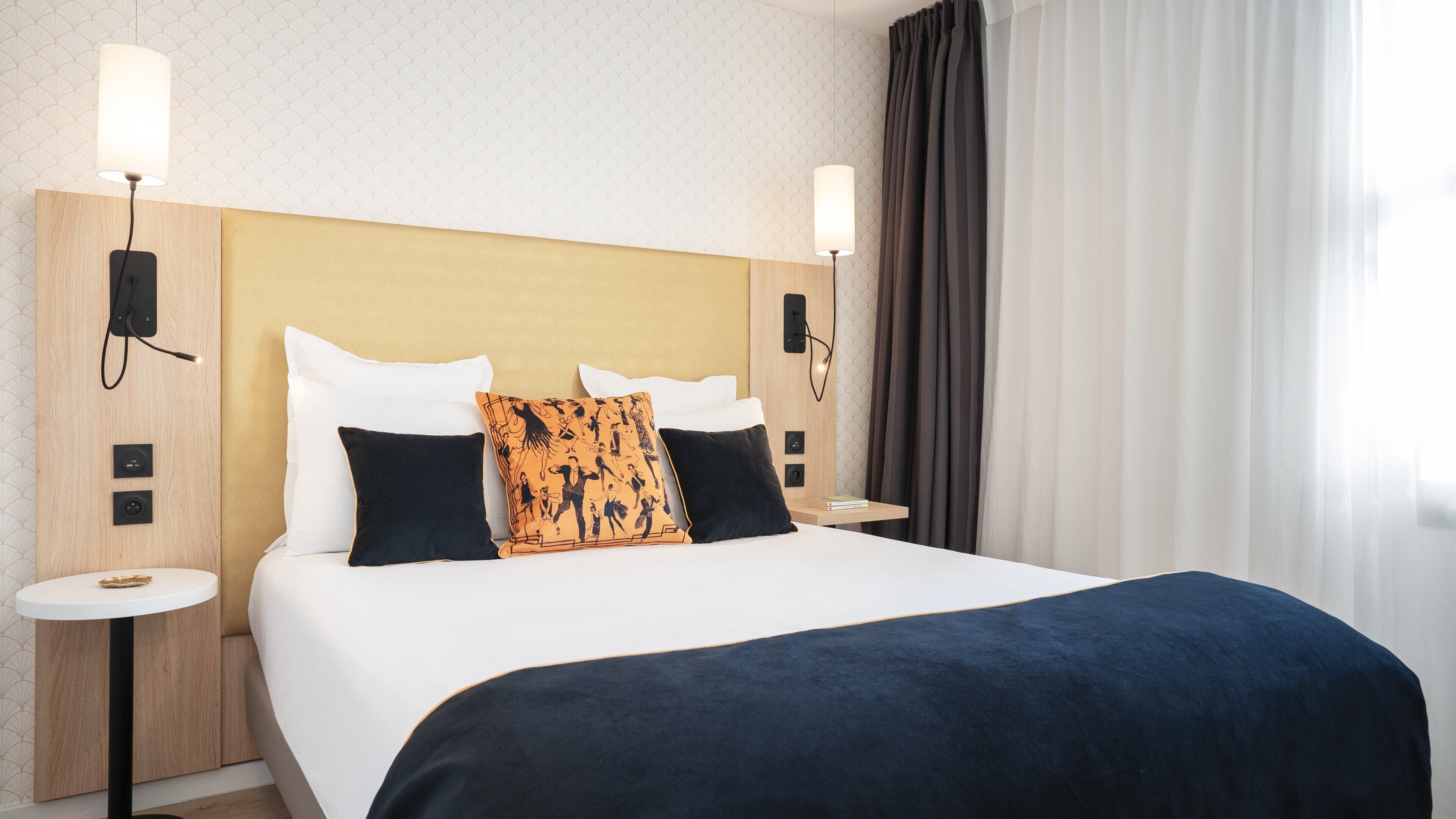 A hotel room with a large bed, two bedside tables, a nightstand, a wall-mounted lamp, and a window with curtains.