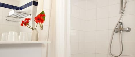 A bathroom with a white sink, mirror, and shower. There are red flowers in a vase on the counter.
