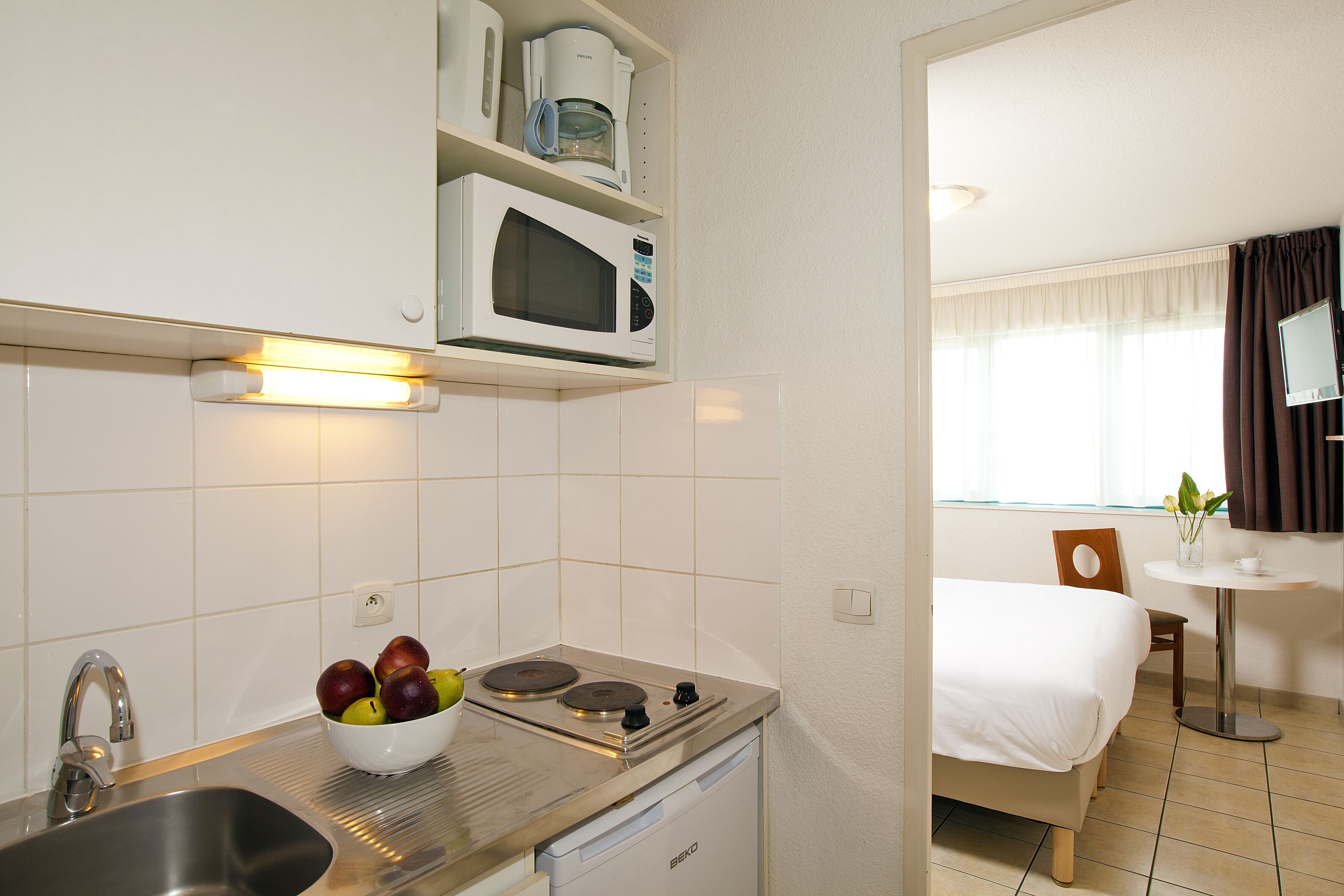 Una cocina compacta con microondas, estufa y lavamanos. Un cuenco con fruta está sobre la encimera.