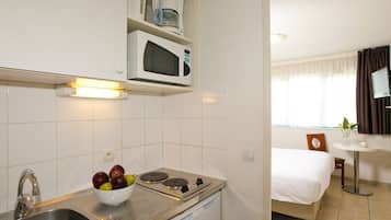 Una cocina compacta con microondas, estufa y lavamanos. Un cuenco con fruta está sobre la encimera.