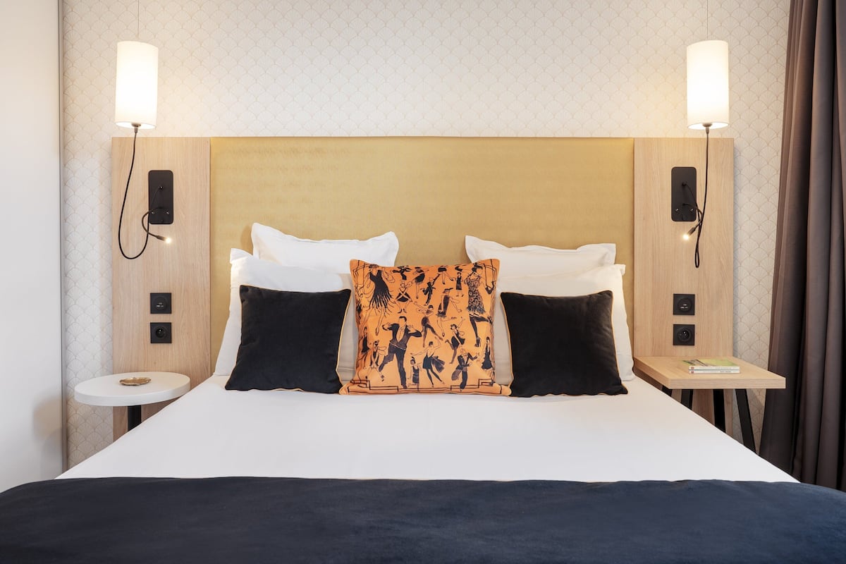 A hotel room with a bed, two bedside lamps, a nightstand, and a wall-mounted phone.