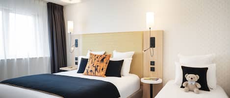 Habitación de hotel con una cama grande, dos mesitas de noche, una lámpara y un osito de peluche sobre una de las camas.