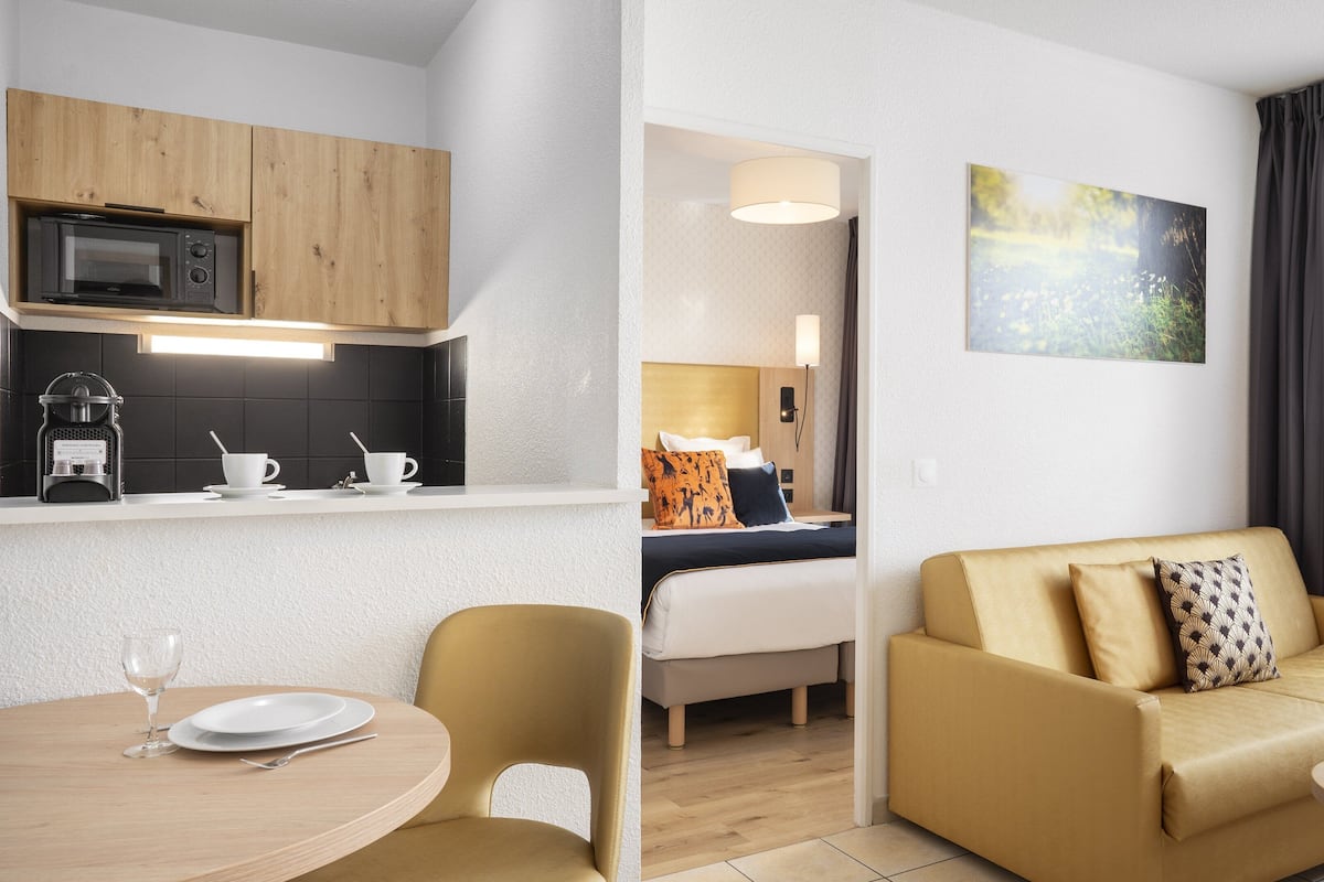 A modern hotel room with a kitchenette, a dining area, a sofa, and a bed.