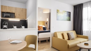 Una habitación de hotel moderna con kitchenette, zona de comedor, sofá y cama.