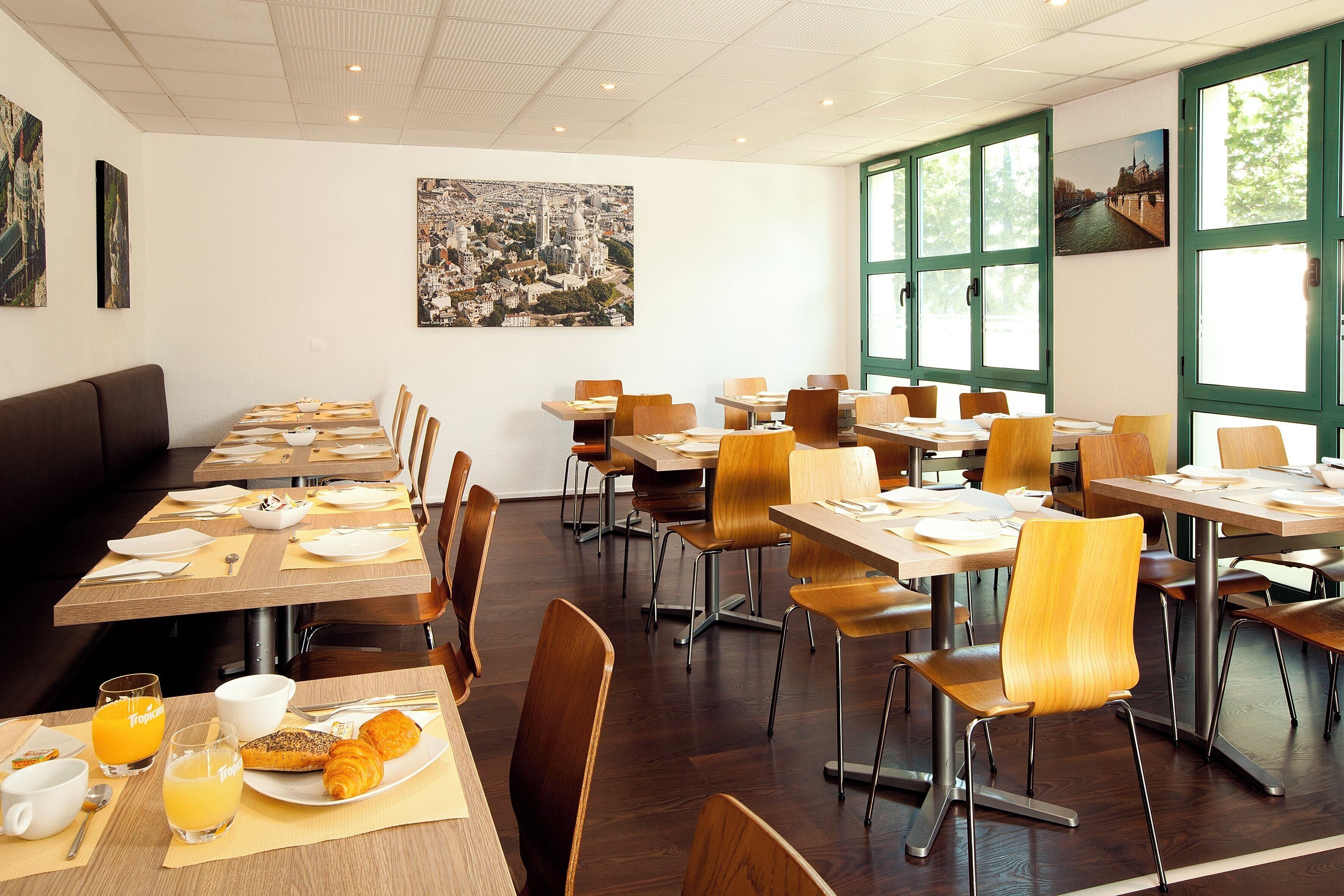 Un comedor con varias mesas y sillas, alimentos para el desayuno sobre las mesas y grandes ventanales con vistas.