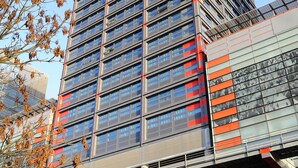 A modern high-rise building with multiple floors, large windows, and a prominent red and gray color scheme.