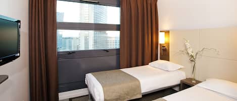 Habitación de hotel con dos camas, televisión, ventana con cortinas, lámpara de noche y un florero con flores.