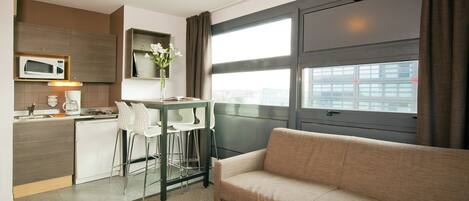 Una habitación de hotel moderna con kitchenette, un sofá y un ventanal grande.