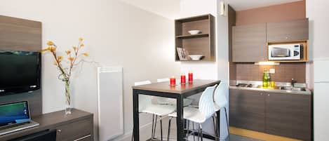 A compact kitchen with a microwave, a small refrigerator, and a dining area with a table and chairs.