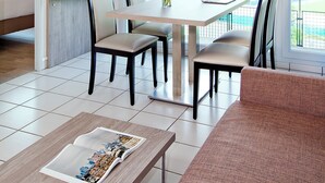 A modern living room with a dining area, a flat-screen TV mounted on the wall, a laptop on the dining table, and a sofa. - Séjours & Affaires Clermont-Ferrand Park Republique (Clermont-Ferrand)