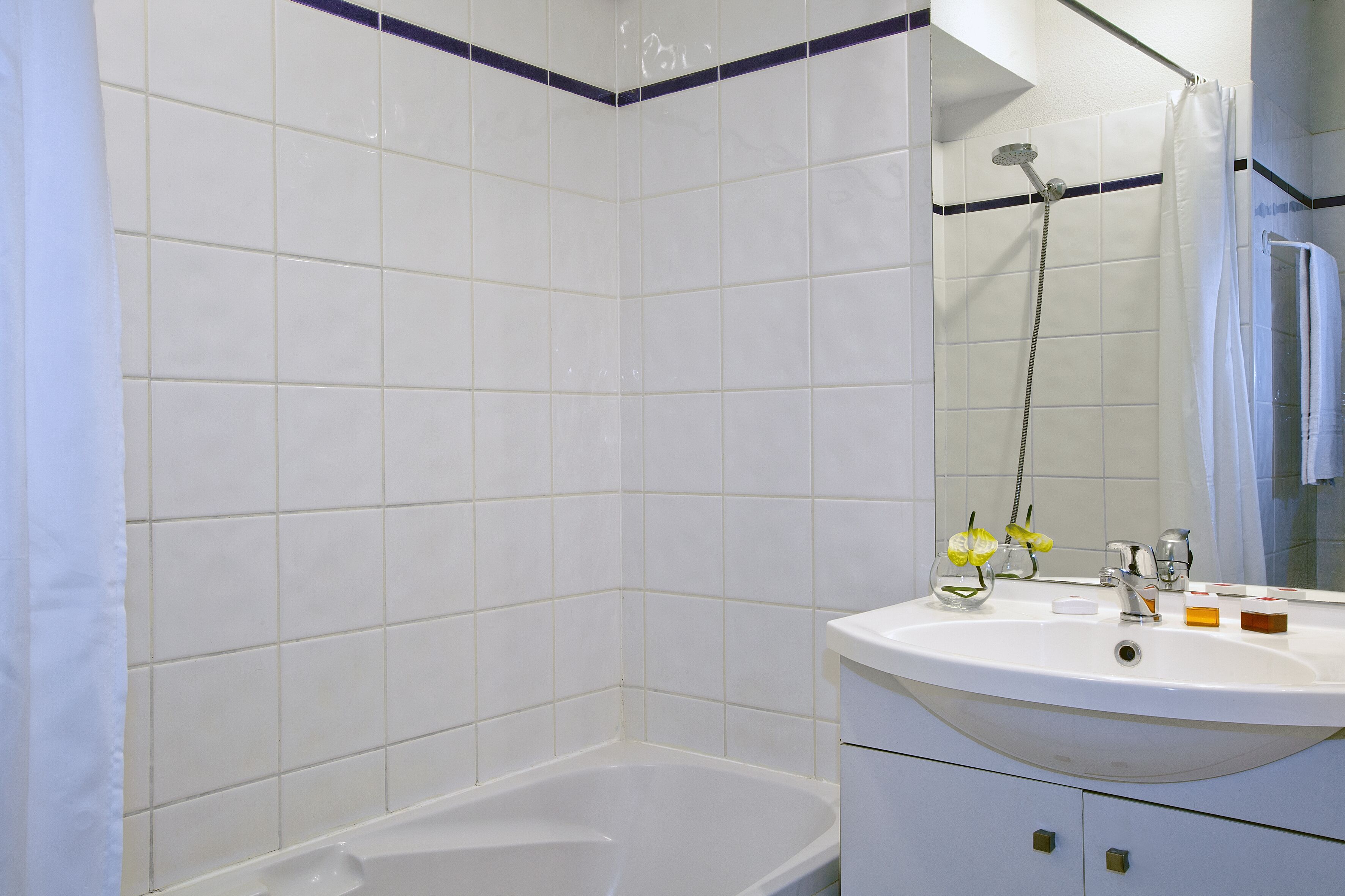 Un baño con azulejos blancos, una bañera, un lavabo con artículos de aseo y una ducha.