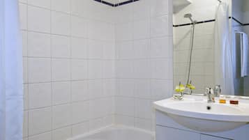 Un baño con azulejos blancos, una bañera, un lavabo con artículos de aseo y una ducha.
