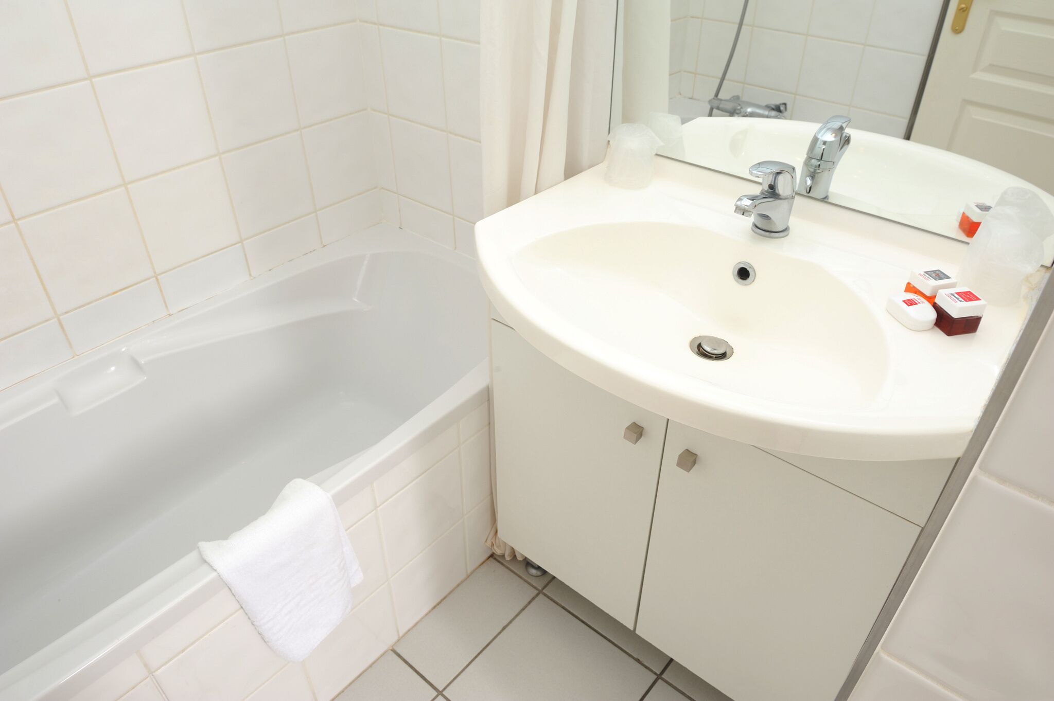 Un baño con una bañera blanca, un lavabo con espejo y artículos de aseo sobre el lavabo.