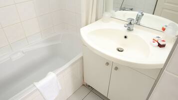 A bathroom with a white bathtub, a sink with a mirror, and toiletries on the sink.