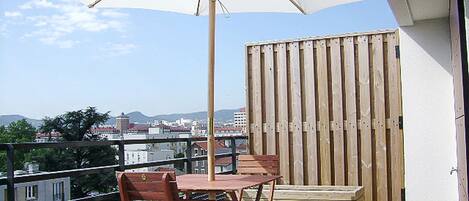 Un balcón con mesa y sillas de madera, una sombrilla y vistas de la ciudad.