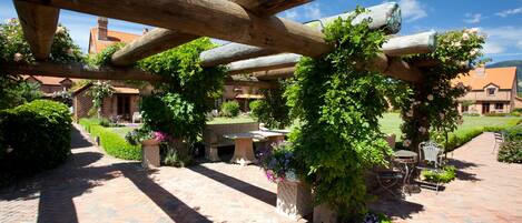 An outdoor patio area with a wooden pergola, brick flooring, and a seating arrangement with a table and chairs.
