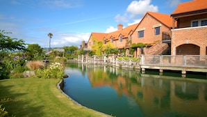 A brick building with a pond in front, a wooden bridge, and a well-maintained lawn. - Grand Arden Monaco Nelson (Nelson)