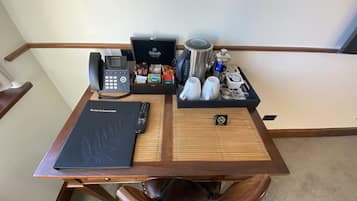 Un escritorio de madera con una carpeta negra que dice “Información de Huéspedes”, un teléfono, una cafetera y una bandeja con tazas y aderezos.