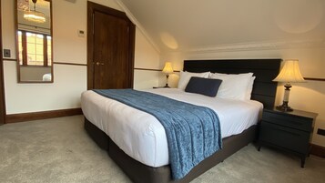 Un lit bien fait, recouvert d’une couverture bleue, avec deux lampes de chevet et une tête de lit en bois foncé.