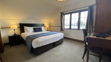 Una habitación de hotel con una cama grande, dos mesitas de noche con lámparas, un escritorio con silla y una ventana que ofrece vistas a palmeras.
