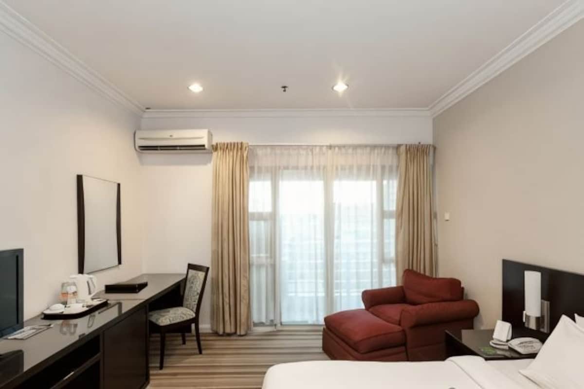 Una camera d'albergo con un letto, una scrivania con una sedia, una televisione e una finestra con tende.