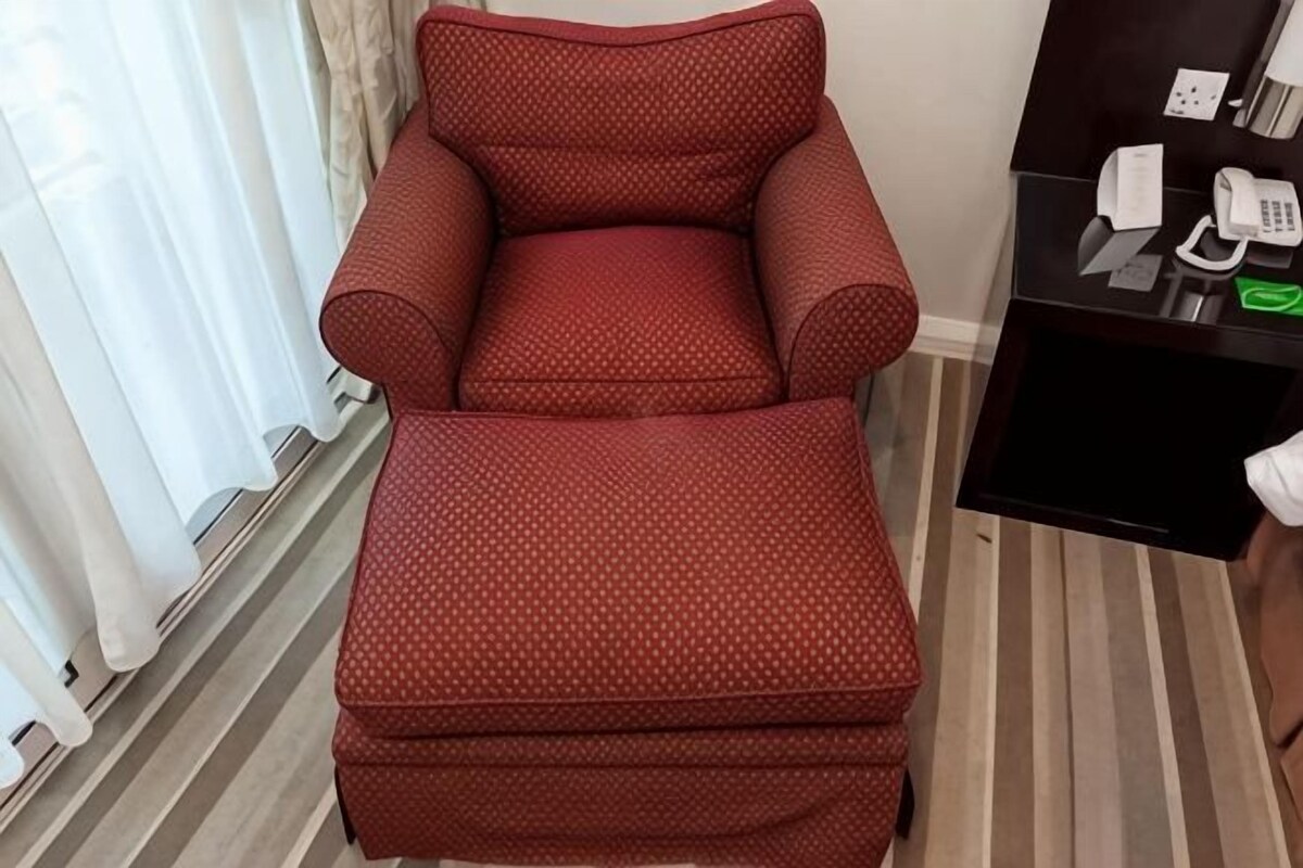 A red upholstered chair and ottoman in a room with a striped floor, a desk with a telephone, and a window with curtains.