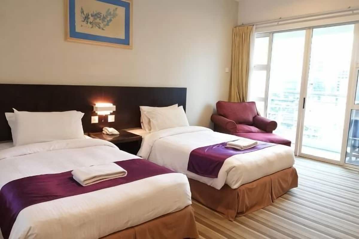 Hotellihuone, jossa on kaksi sänkyä, yöpöytä lampun kanssa, tuoli ja suuri ikkuna, josta on näkymä.