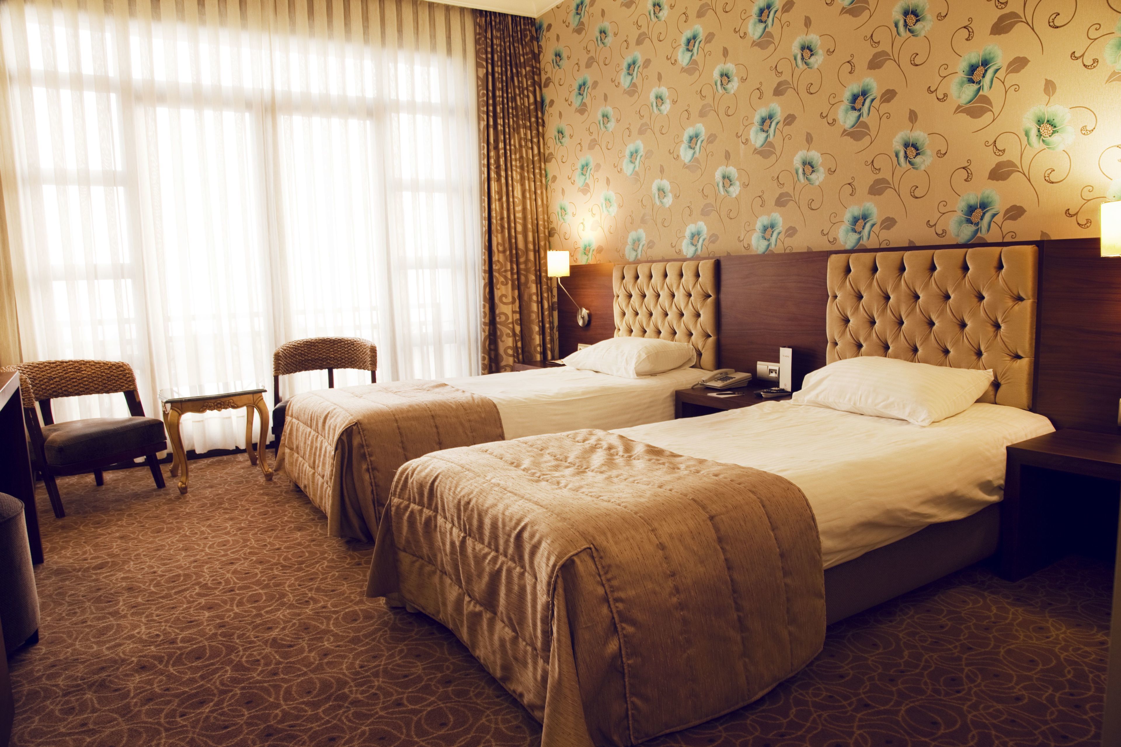 Quarto de hotel com duas camas, uma cadeira, uma mesa e um abajur.