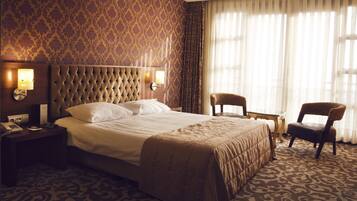 Habitación de hotel con una cama grande, dos mesitas de noche, una silla y una ventana con cortinas.