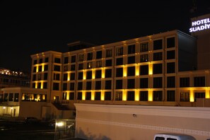 Un hôtel à plusieurs étages, avec des fenêtres illuminées et une enseigne indiquant « HÔTEL SUADİY ».
