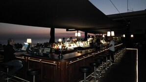 Zona de bar con una barra larga, taburetes y vista al océano al atardecer.