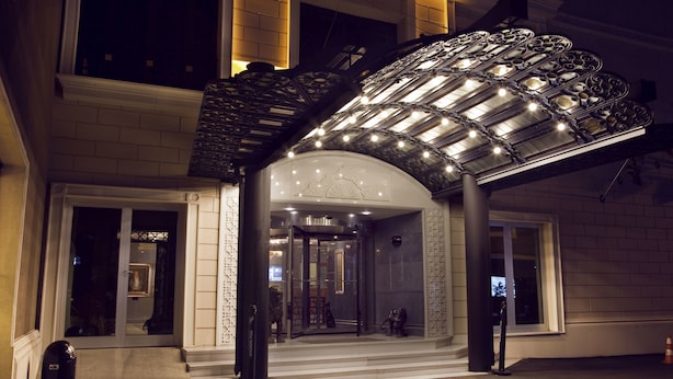Entrada de hotel con puerta de vidrio, zona de acceso cubierta y escalera que lleva al piso superior.