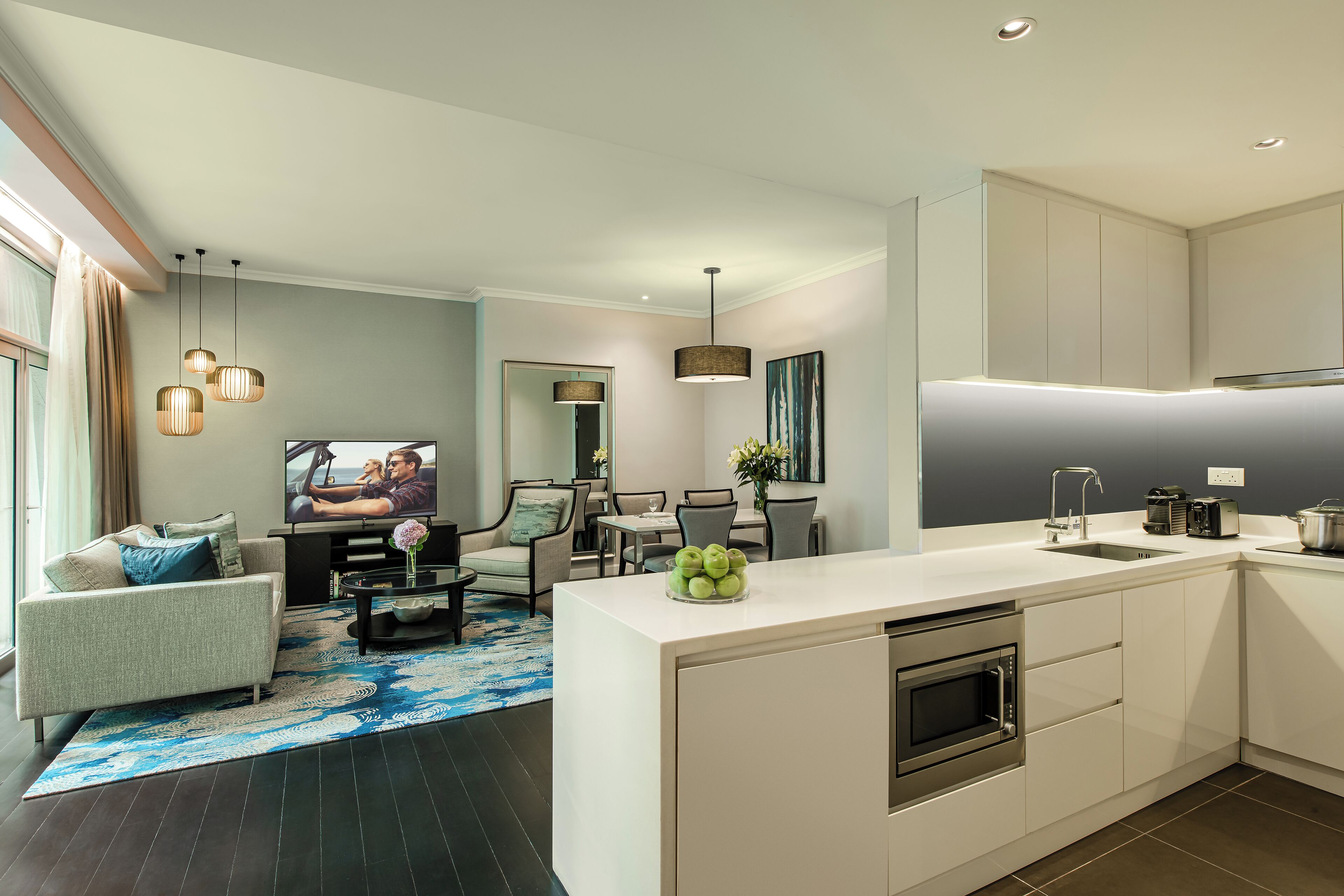 A modern kitchen with a central island, built-in oven, and a dining area with chairs and a table.