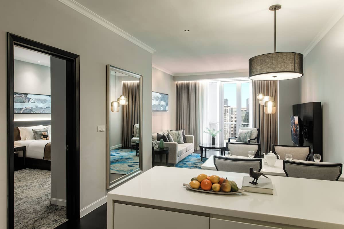 Une chambre d’hôtel moderne dotée d’un coin repas, d’un espace de vie et d’une grande fenêtre offrant une vue sur la ville.