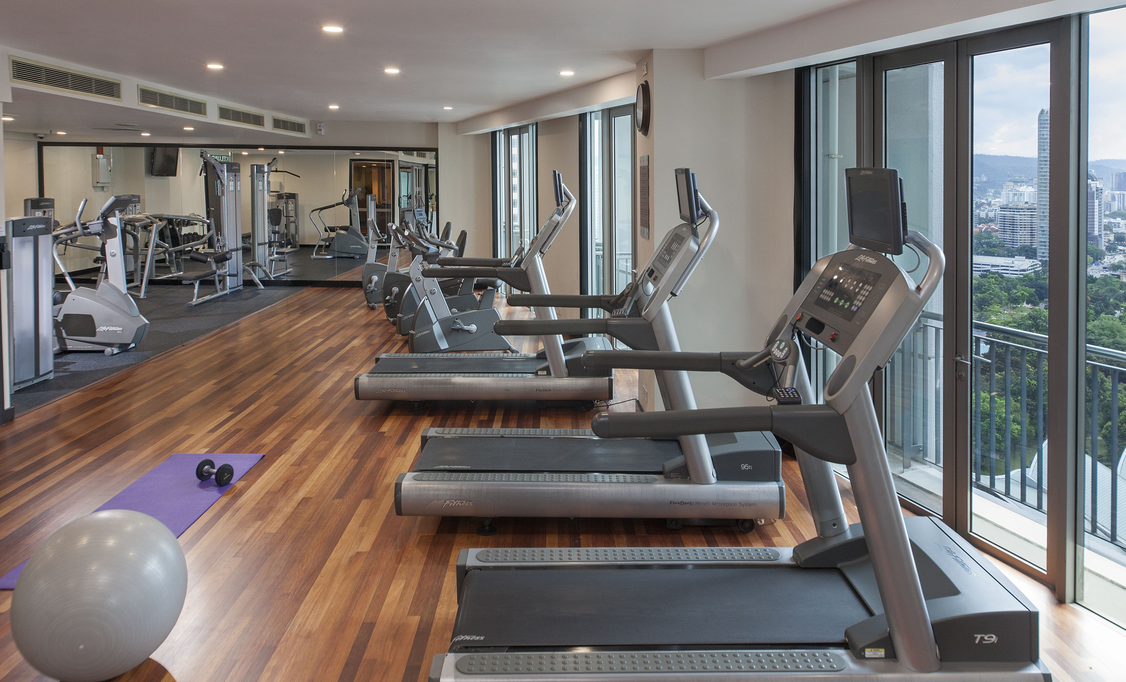 Une salle de sport équipée de plusieurs tapis de course, de ballons d’exercice et d’un tapis violet.