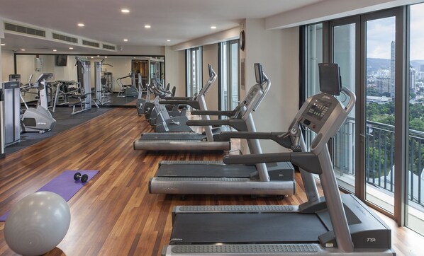 Un gimnasio con cintas de correr, pelotas de ejercicio y una colchoneta morada.