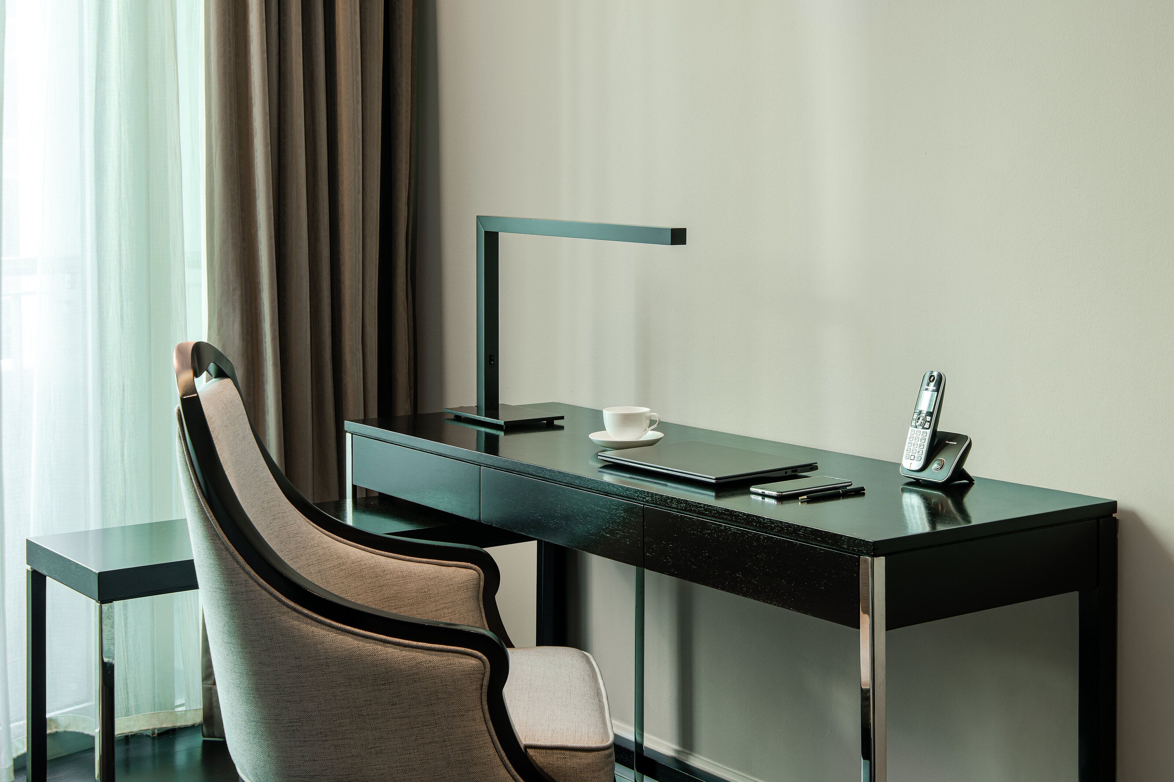 A modern hotel room with a glass desk, a chair, a telephone, and a cup.