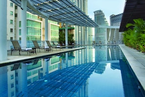Una piscina infinita en la azotea con sillones de descanso y vistas de edificios altos circundantes.