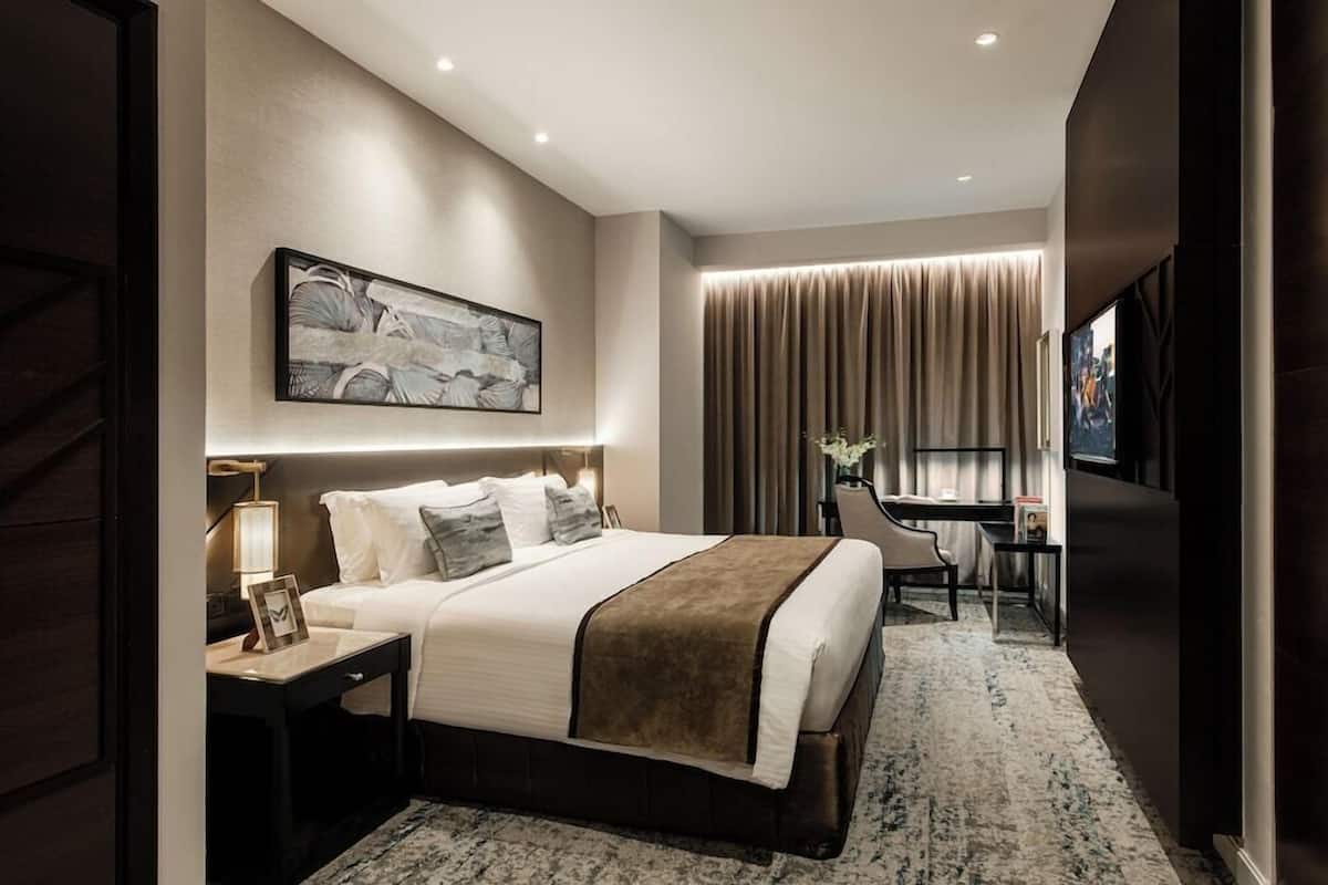 Une chambre d’hôtel moderne équipée d’un grand lit, d’une table de chevet, d’un bureau, d’une chaise et d’un téléviseur.