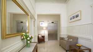 A hotel lobby with a reception desk, two elevators, a sofa, a small table with fruit, and a vase with flowers. - Hotel Sophia (Melbourne)