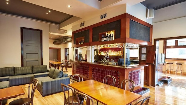 A bar area with a wooden counter, bar stools, and a seating area with a sofa and tables. - Hotel Sophia (Melbourne)