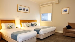 A hotel room with two beds, a sofa, and a window with blinds. - Hotel Sophia (Melbourne)