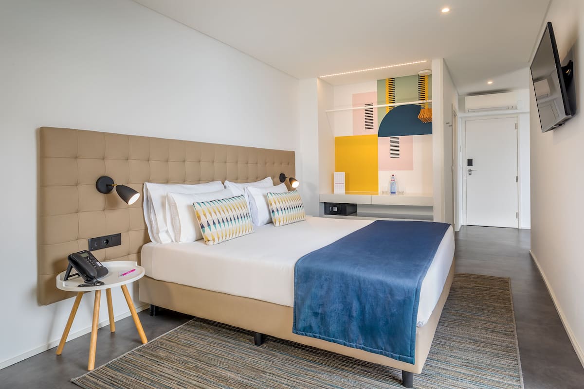 A modern hotel room with a large bed, bedside table with a phone, and a TV mounted on the wall.