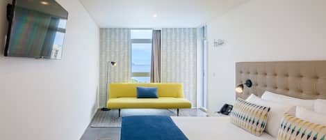 Une chambre d’hôtel moderne avec un grand lit, un canapé jaune et une vue sur la mer.