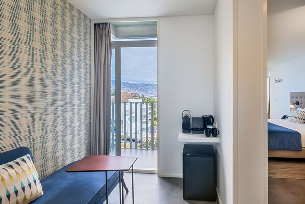 Una habitación de hotel con un ventanal grande, una cama, un escritorio con silla y una mesita.