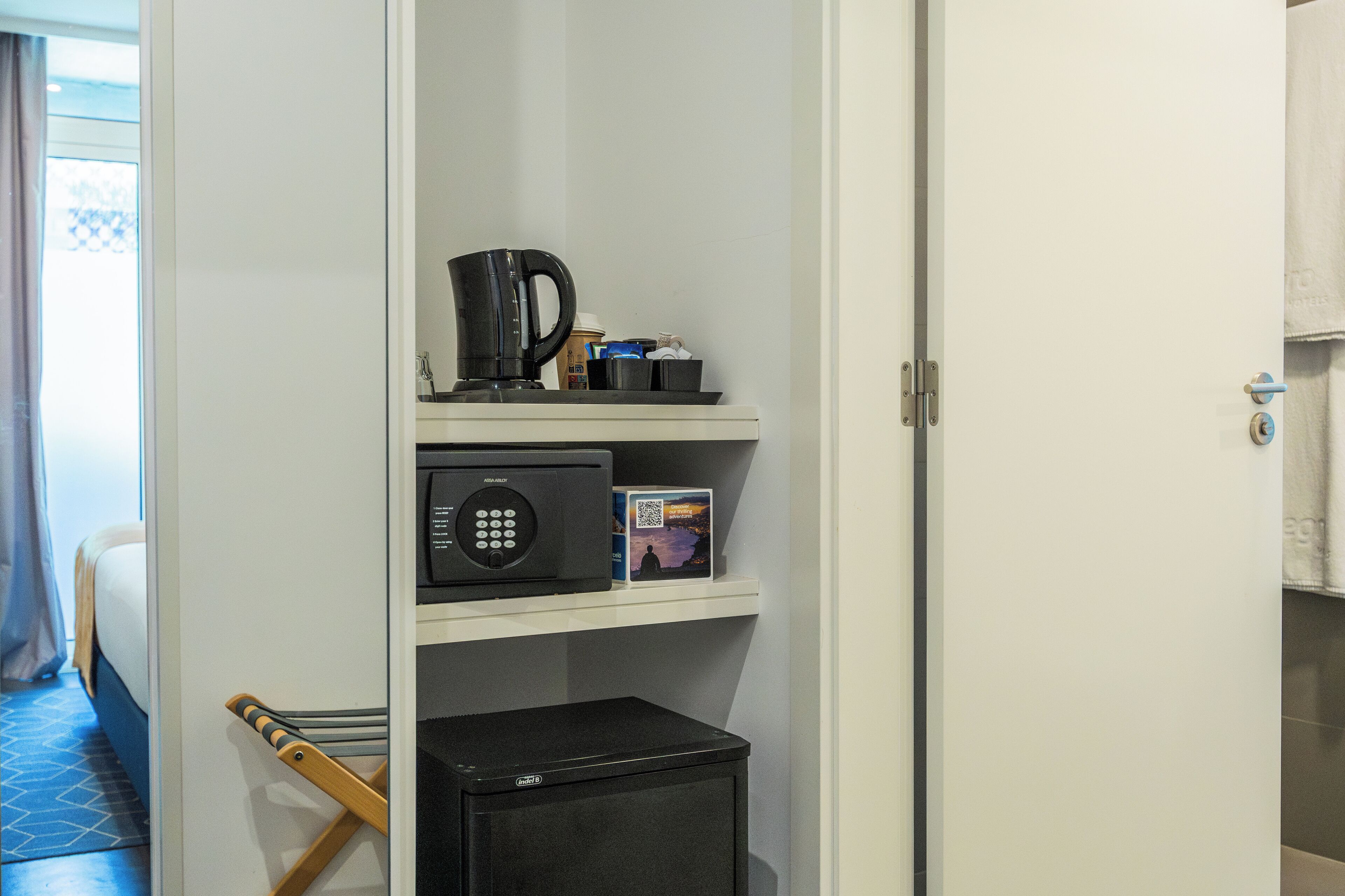 A hotel room with a microwave, coffee maker, and a small refrigerator on a white shelf.