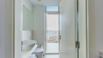 A modern bathroom with a white sink, toilet, and a glass door leading to a balcony.