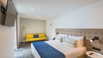 Una habitación de hotel moderna con una cama grande, un sofá amarillo, un televisor y una mesita.