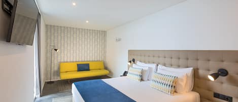 A modern hotel room with a large bed, a yellow sofa, a TV, and a small table.